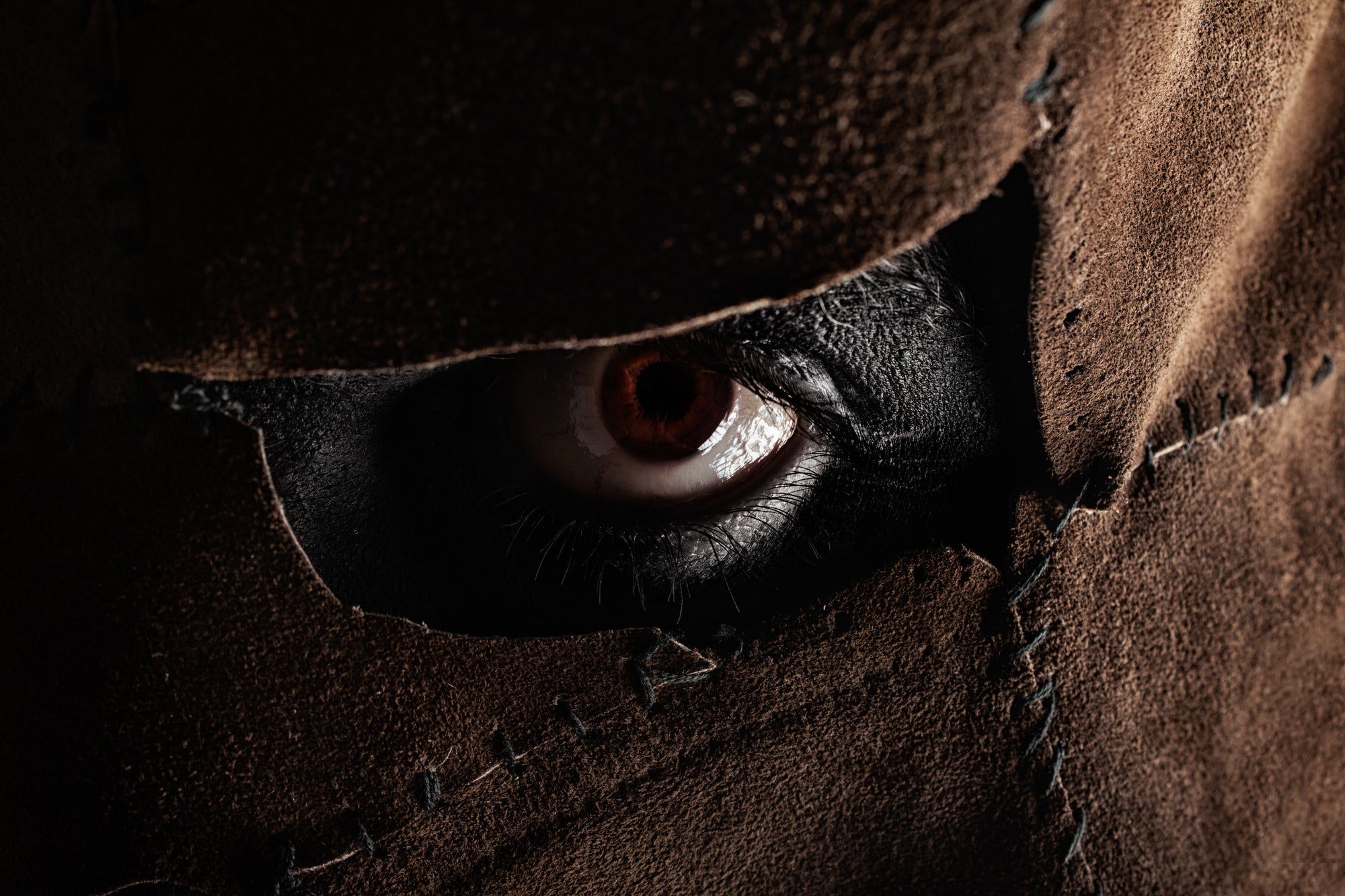 A close-up picture of Leatherface’s eye in his mask.
